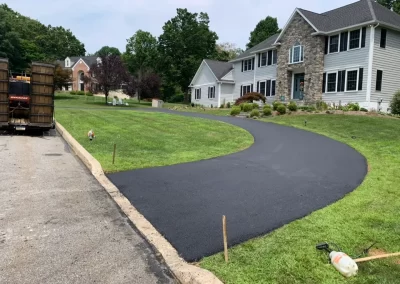 A freshly paved black asphalt driveway by Asphalt Worxx LLC curves up to a large suburban house with a stone facade in Toms River, New Jersey.