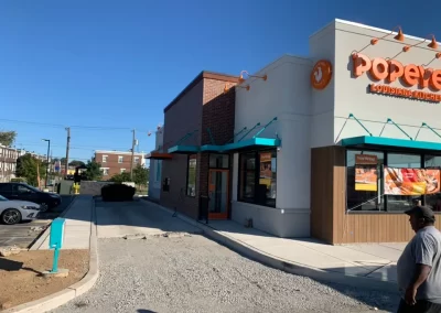 A Popeyes drive-thru in New Jersey ends abruptly in gravel instead of smooth asphalt before reaching the order window; a man stands nearby.