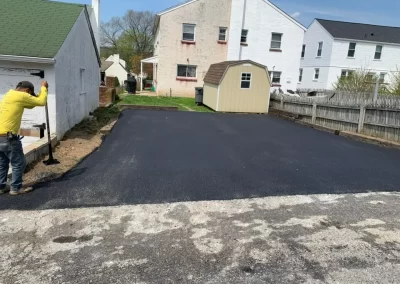 A worker stands by a newly paved black asphalt driveway in a residential Toms River, New Jersey backyard, showcasing the quality craftsmanship of Asphalt Worxx LLC.