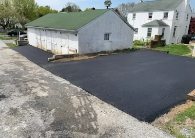 A freshly paved black asphalt driveway sits beside a white building with a green roof in Toms River, New Jersey, on a clear day.