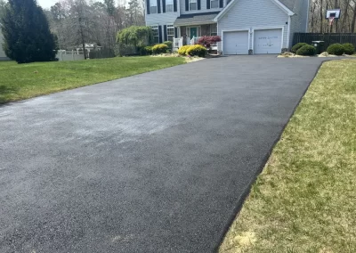 A freshly paved asphalt driveway by Asphalt Worxx LLC enhances a suburban Toms River home, bordered by a lush green lawn.