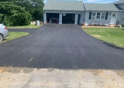 Freshly paved black asphalt driveway, a testament to quality asphalt services in New Jersey, leads to the two-car garage of a suburban house.