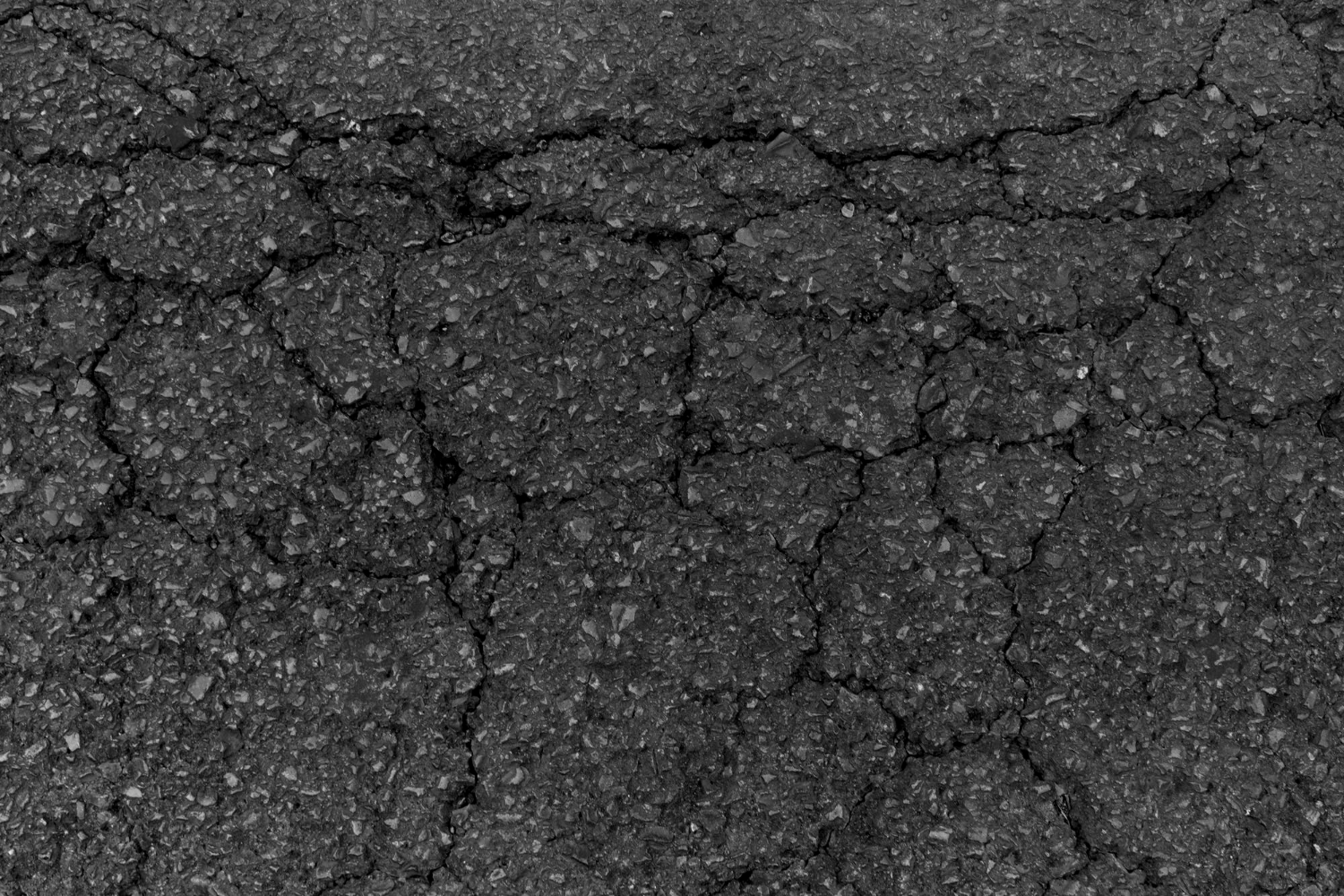 Cracked asphalt surface with visible rough texture and multiple intersecting fissures.